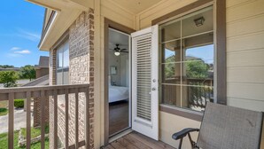 Un porche cubierto con terraza de madera, una puerta corrediza de vidrio que da a un dormitorio y una silla.