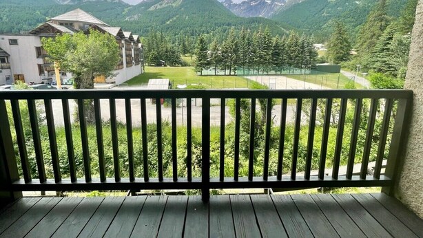 Un balcon donnant sur un paysage montagneux, une zone herbeuse et un bâtiment doté d’un toit en pente.