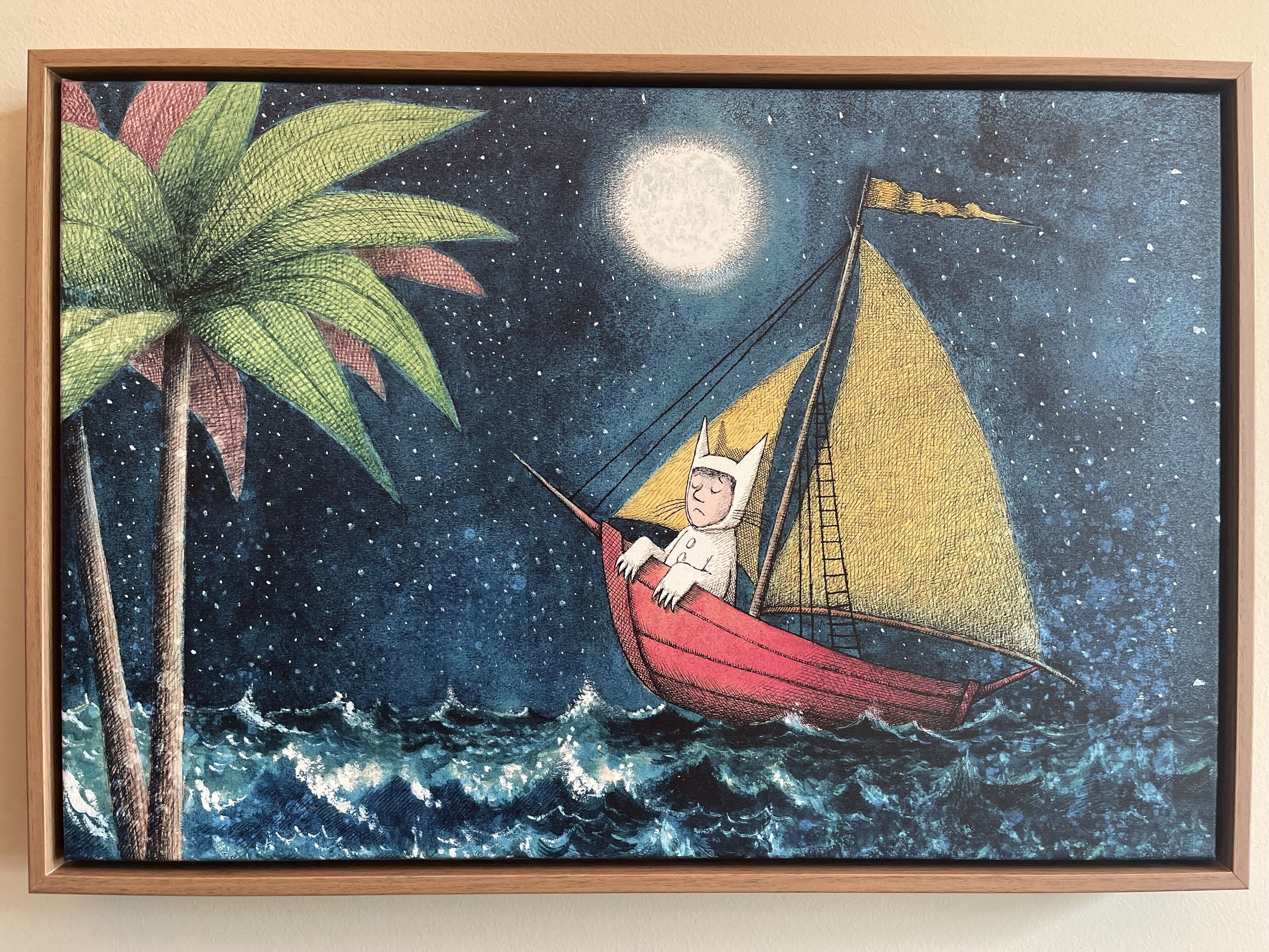 A framed artwork of a cat in a boat on a moonlit night with a palm tree.