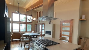 A modern kitchen with wooden flooring, a central island, and a dining area with chairs. - Wild Thing - Blowing Rock, Hot Tub, Big Views, NEW (Lenoir)