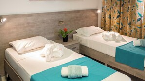 A hotel room with two beds, a nightstand with a lamp, a potted plant, and a bathroom with a shower curtain. - Comfort Studio Apartment Combined Living, Bedroom and Kitchen as seen in photo (San Pawl il-Bahar)