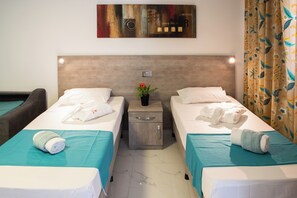A hotel room with two single beds, a nightstand with a vase of flowers, and a painting on the wall. - Comfort Studio Apartment Combined Living, Bedroom and Kitchen as seen in photo (San Pawl il-Bahar)