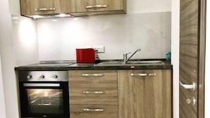 A kitchen with wooden cabinets, a stainless steel oven, and a red appliance on the countertop. - Comfort Studio Apartment Combined Living, Bedroom and Kitchen as seen in photo (San Pawl il-Bahar)