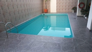 Ein rechteckiger Innenpool mit klarem, blauem Wasser, umgeben von grauen Marmorböden und Wänden mit Mosaikmuster.