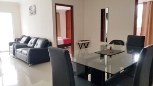 Ein modernes Hotelzimmer mit einem Glastisch, schwarzen Ledersofas und einem Bett mit roter Bettdecke.