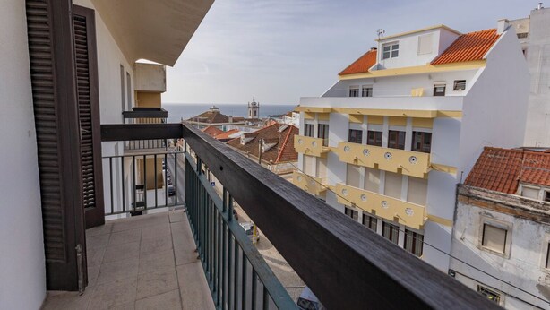 Un balcón con vista a un pueblo costero, con edificios de techos rojos y un cielo despejado.