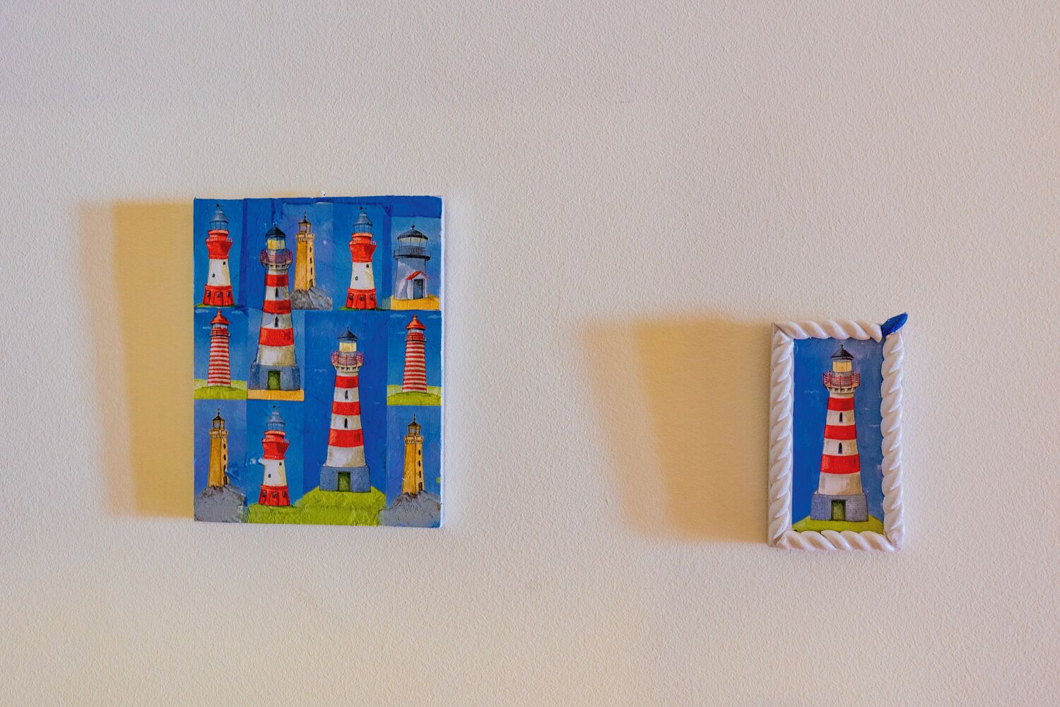 Two framed artworks of lighthouses on a wall.