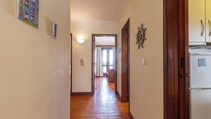 Un pasillo con piso de madera, un refrigerador y una puerta que da a otra habitación.