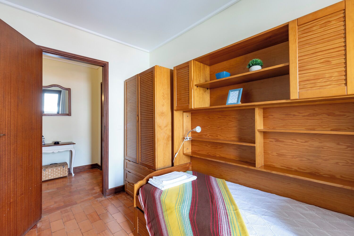 A bedroom with a bed, wooden wardrobe, and a desk with a chair.