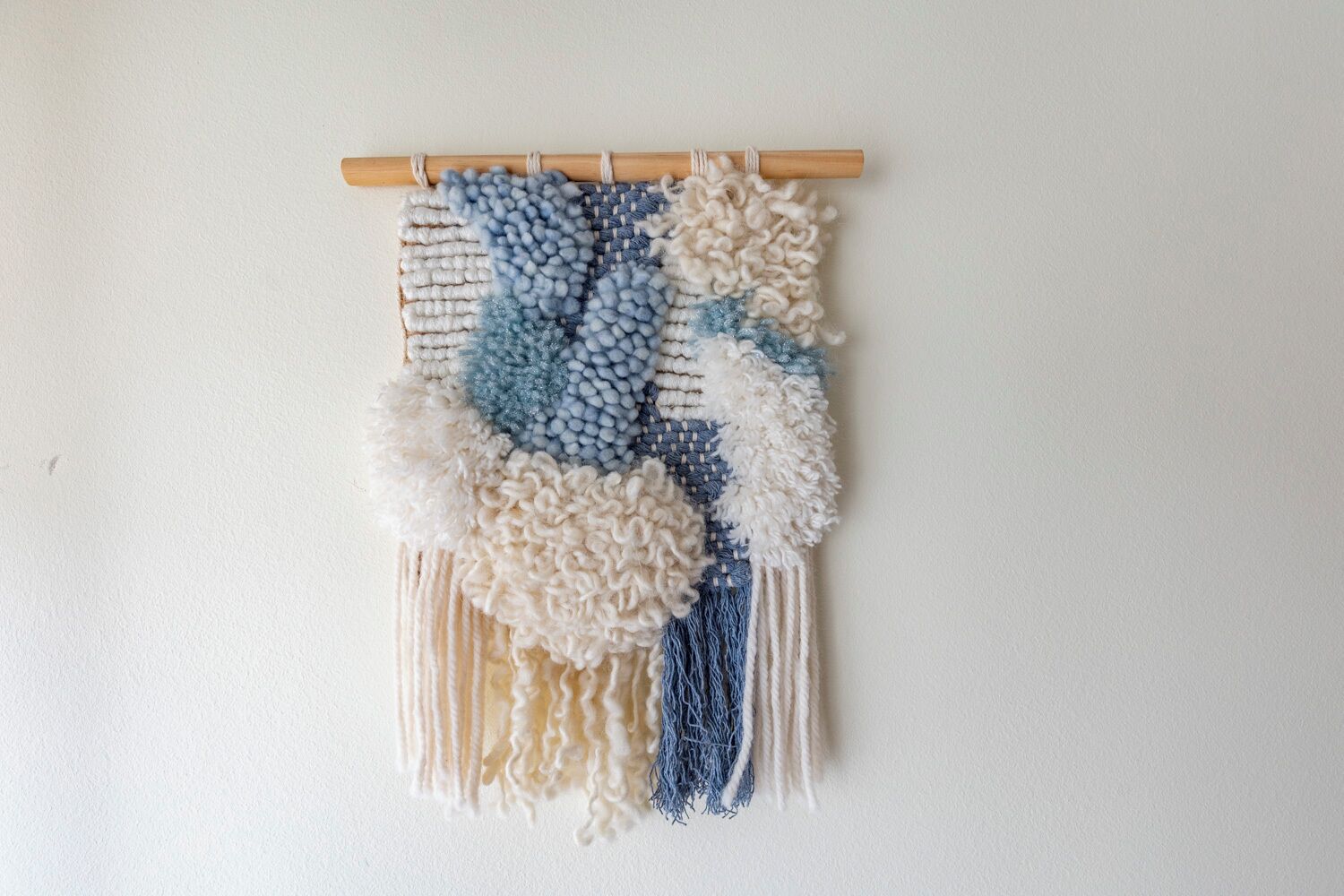 Wandtegoed met een houten lat, voorzien van een macramé ontwerp in blauw en wit garen.