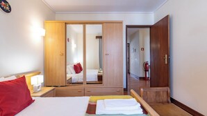 Una habitación de hotel con cama, mesita de noche con lámpara, armario y espejo.