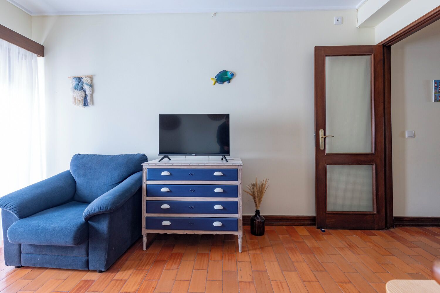 A living room with a blue sofa, a wooden TV stand with a flat-screen TV, a wooden door, and a small wall decoration.