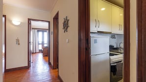 Un pasillo que conduce a una cocina con piso de madera, un refrigerador y una estufa.