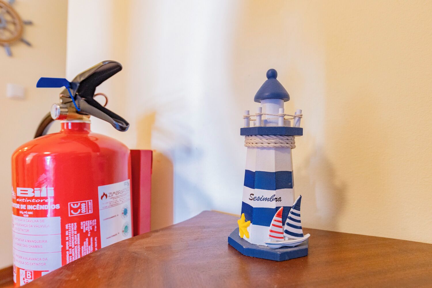 A red fire extinguisher and a small lighthouse model on a wooden table.