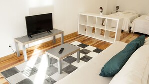 Un soggiorno moderno con una televisione a schermo piatto, un tavolino da caffè, un divano con un cuscino color petrolio e una libreria bianca.