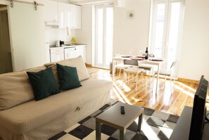 Un salon comprenant un canapé, une table basse et un téléviseur. Il y a également un coin repas avec une table et des chaises.