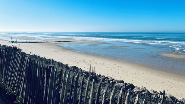 Una playa con una cerca de madera en primer plano y un cielo azul despejado.
