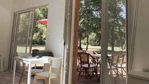 Una habitación con puerta corredera de vidrio que da a un patio exterior con mobiliario de mimbre y un paraguas rojo.