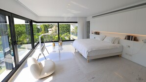 Een moderne slaapkamer met een groot bed, een witte stoel en uitzicht op groen.
