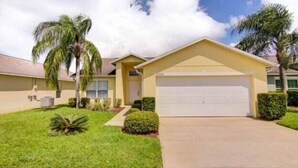A single-story house with a garage, surrounded by well-maintained lawns and palm trees. - Lake View Villa. Peaceful, 3 bed family home away from home. (Clermont)