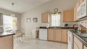 A kitchen with wooden cabinets, a dishwasher, a microwave, and a dining area with chairs and a table. - Lake View Villa. Peaceful, 3 bed family home away from home. (Clermont)