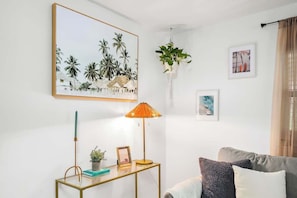 A living room with a sofa, a coffee table with a lamp, a framed picture, and a hanging plant.