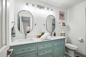 A bathroom with two large mirrors, a white sink, a green vanity, and a toilet.