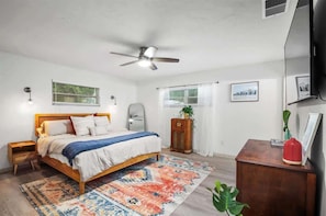 A bedroom with a bed, a ceiling fan, a nightstand, a dresser, and a window with curtains.