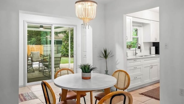 Una cocina moderna con armarios blancos, una mesa redonda con sillas de mimbre y un candelabro.