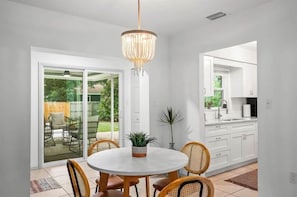 A modern kitchen with white cabinets, a round dining table with wicker chairs, and a chandelier.