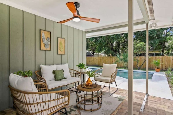 A covered patio area with wicker furniture, a ceiling fan, and a view of a backyard swimming pool.
