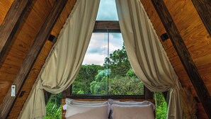 A bedroom with a bed, curtains, and a window with a view of greenery. - Urutau Pousada (Urubici)