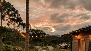 A wooden table with a charcuterie board and two glasses of red wine, set against a scenic backdrop of a house and trees under a twilight sky. - Urutau Pousada (Urubici)