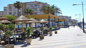 A beachfront promenade with outdoor seating and umbrellas, palm trees, and a clear sky. - Sea View Apt Steps to Beach (Málaga)