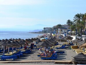Una playa con cabañas de techo de paja y sillas de tomar el sol.