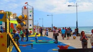 A playground with colorful equipment and a blue mat, located near a beach with people in the background. - Sea View Apt Steps to Beach (Málaga)