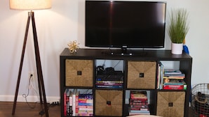 A living room with a television, bookshelves, a lamp, and a round ottoman. - Cozy-Hoosier themed bungalow-Walk to best city parks and Downtown. (Bloomington)