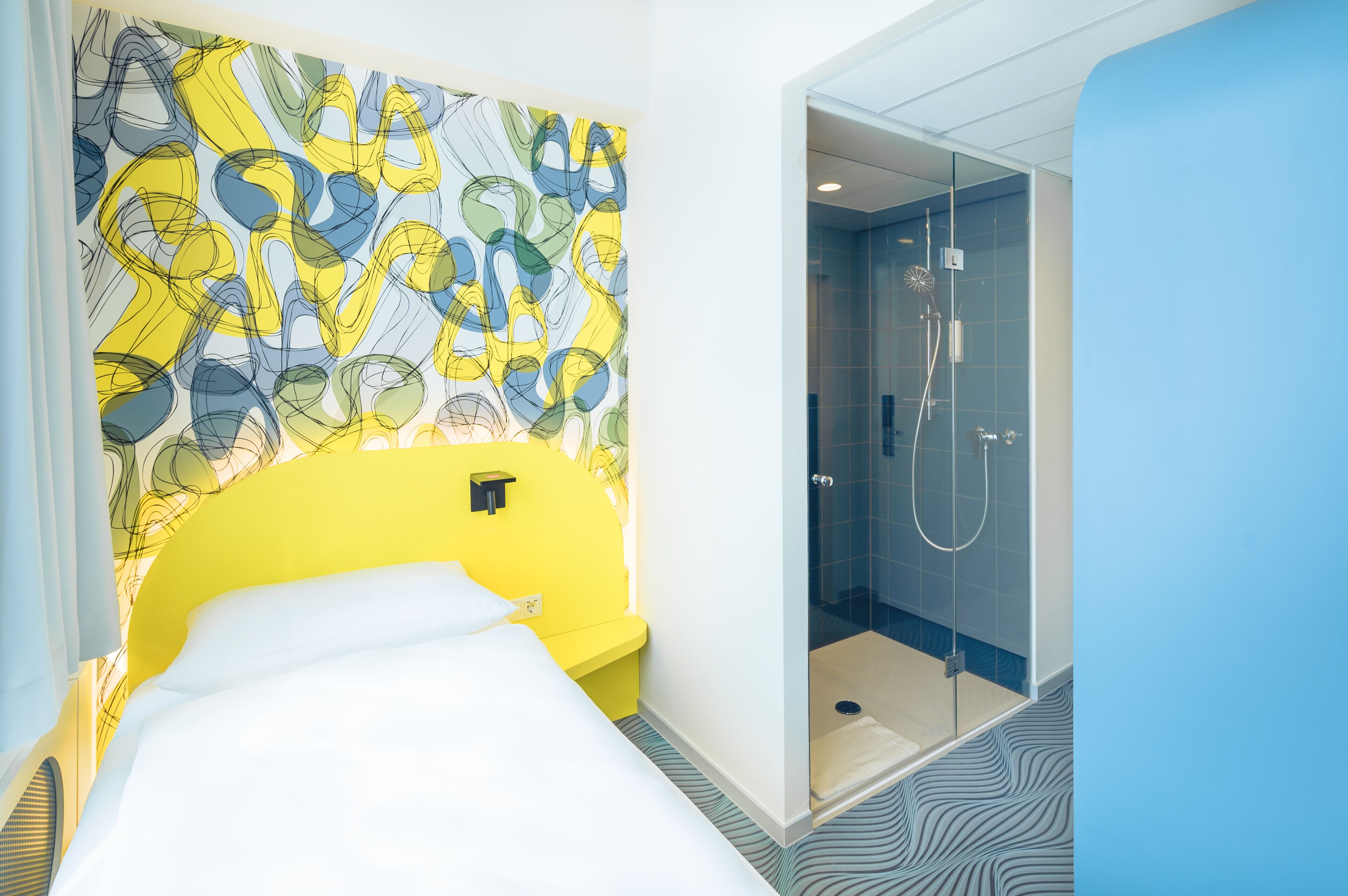 Una habitación de hotel con cama, ducha y una pared decorada con arte abstracto.