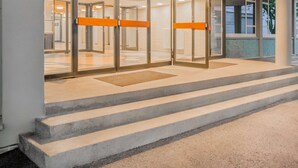L’entrée d’un hôtel, avec une porte en verre, un panneau lumineux indiquant « prizeotel », et un escalier menant à l’entrée.
