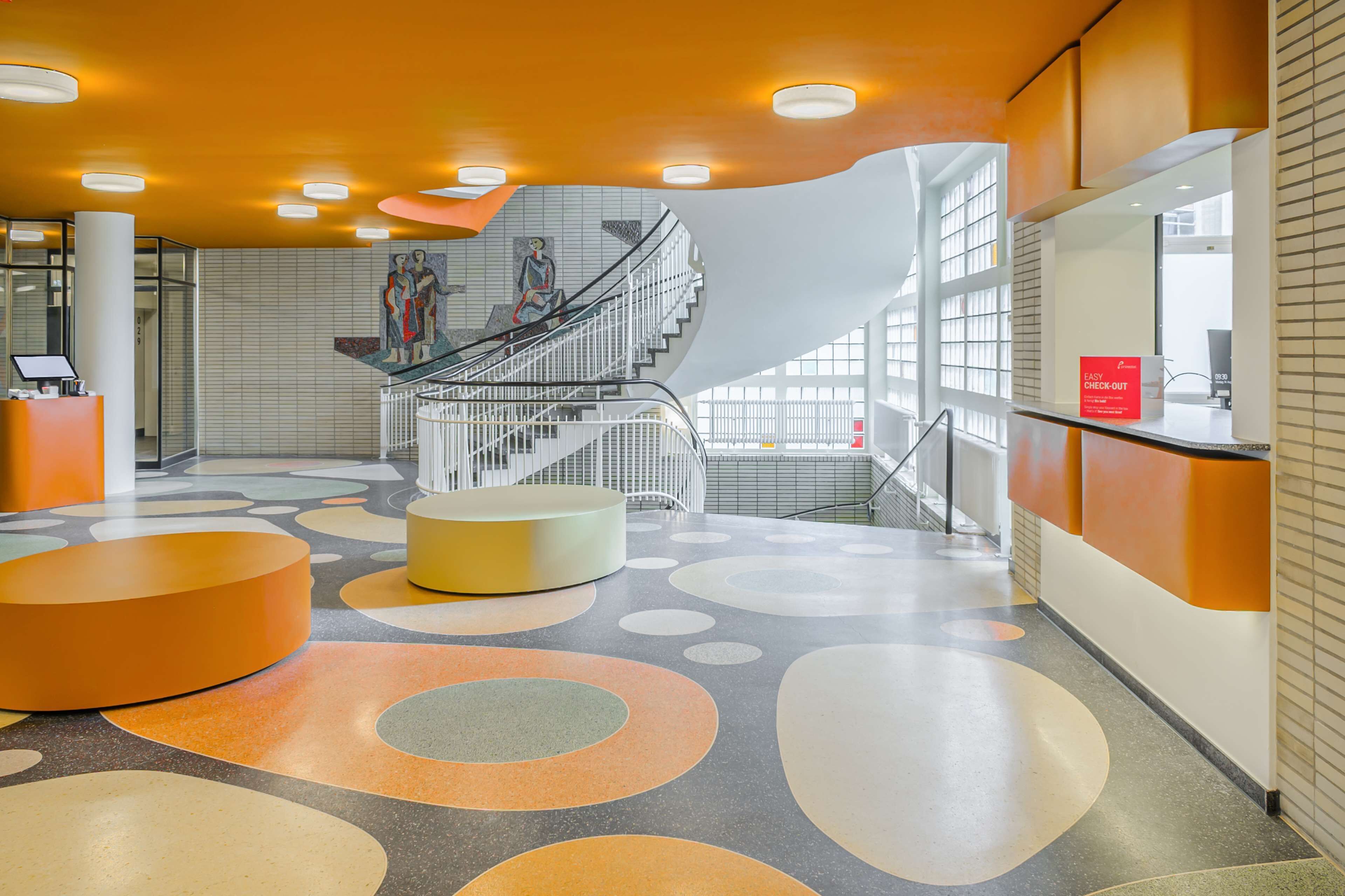 Un hall d’entrée moderne avec un escalier central, un comptoir d’accueil et un sol à motifs.