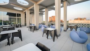 Un espace de restauration aménagé sur le toit, avec des tables et des chaises, de grandes fenêtres et une vue sur les bâtiments au loin.