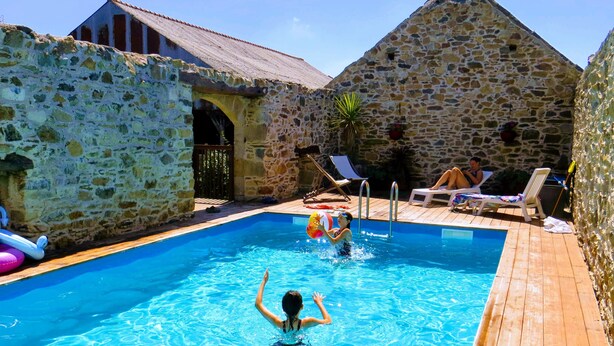 A stone-walled pool area with a wooden deck, lounge chairs, and a person swimming.
