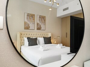 Quarto de hotel com uma cama grande, cabeceira, mesa de cabeceira, espelho e obras de arte na parede.