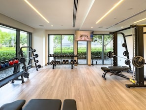 Uma academia com equipamentos de musculação, bancos e uma tela de televisão.