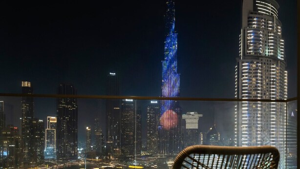 Un balcon avec une table, deux chaises et une vue sur les gratte-ciel de la ville la nuit, notamment le Burj Khalifa.