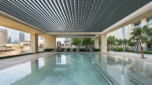 Une piscine au design moderne, entourée de chaises longues et dotée d’un espace abrité avec un plafond à lattes.