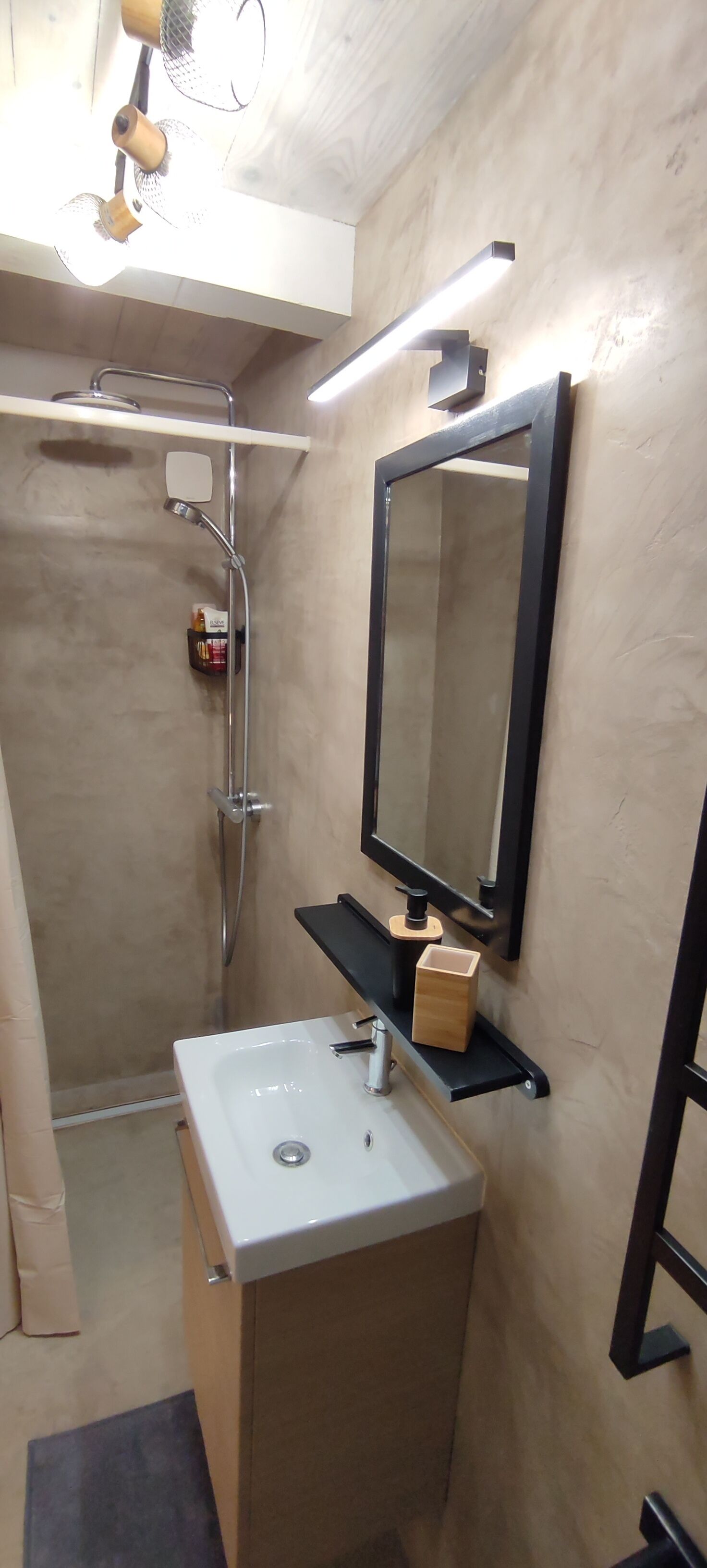 Une petite salle de bain avec un lavabo blanc, un miroir et une douche.
