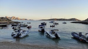 A marina with various boats docked, a rocky shoreline, and distant hills.