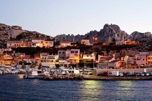 A coastal town with buildings on a hillside, a marina with boats, and rocky cliffs in the background.