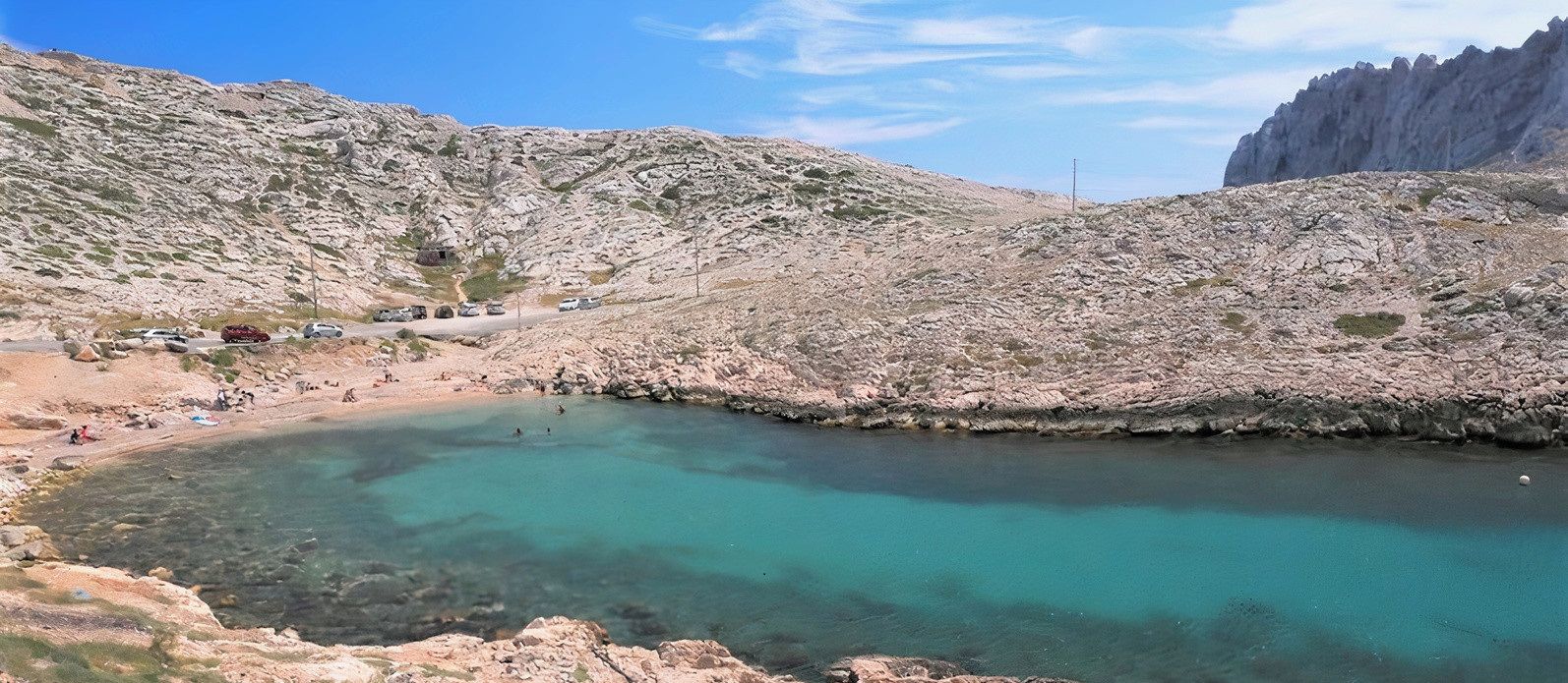 Een rotsachtig landschap met een helder turquoise meer, omgeven door heuvels.